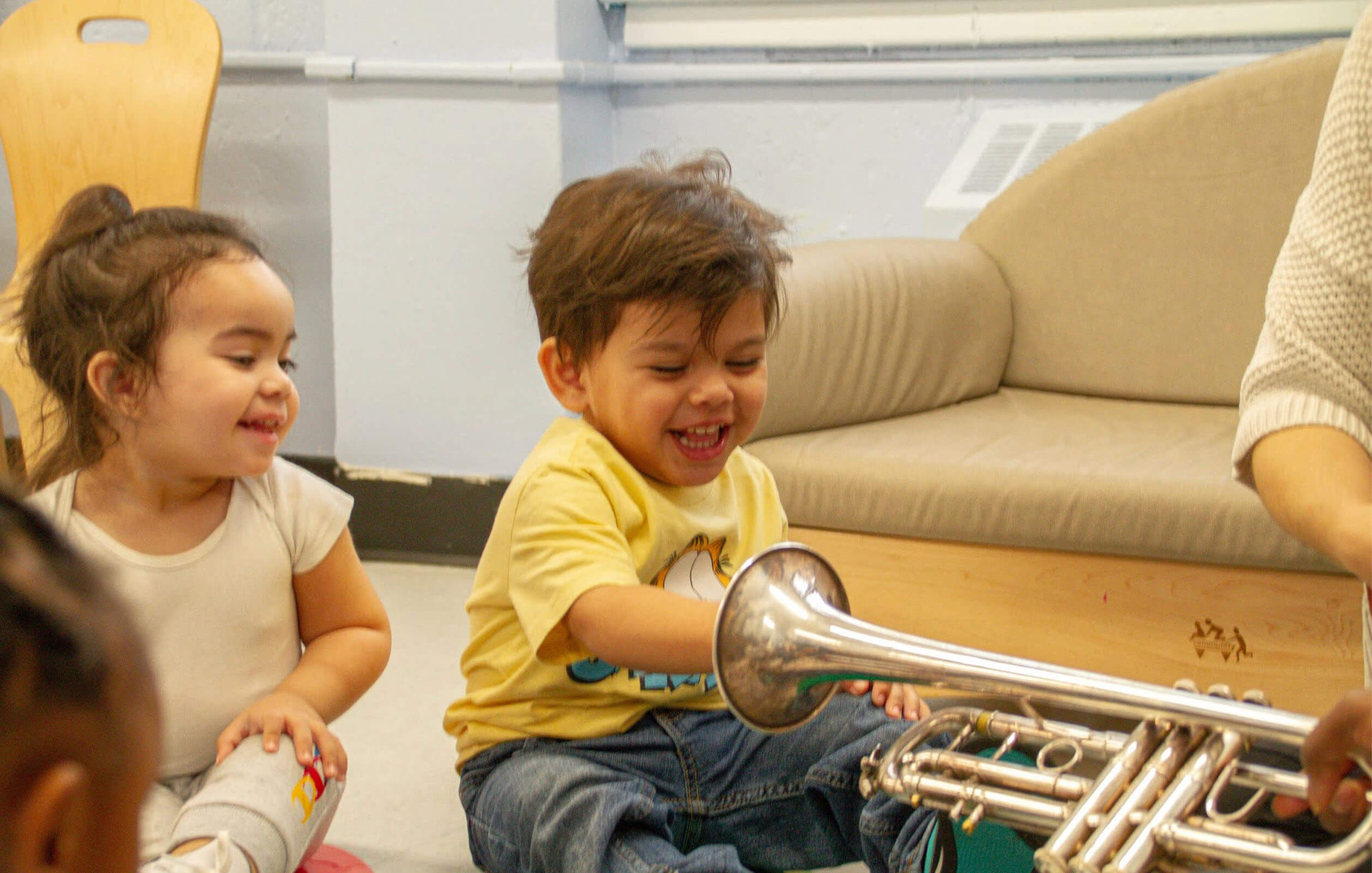 A small child putting his hand inside a trumpet during music class at a Grand Street Settlement daycare center