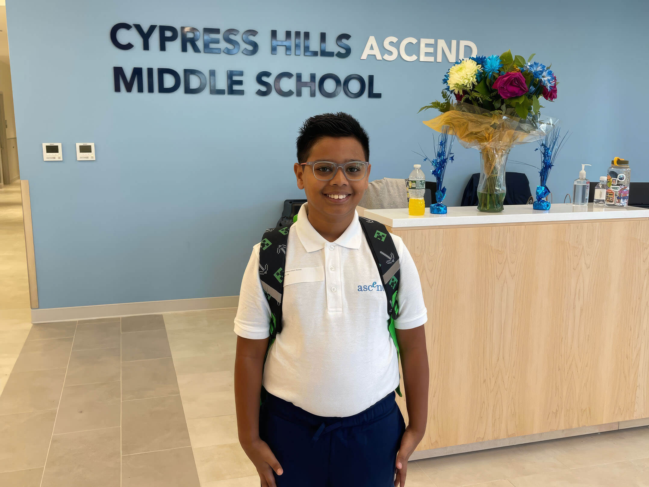 Student posing in front of reception desk at Cypress Hills Ascend Middle School in Brookyn