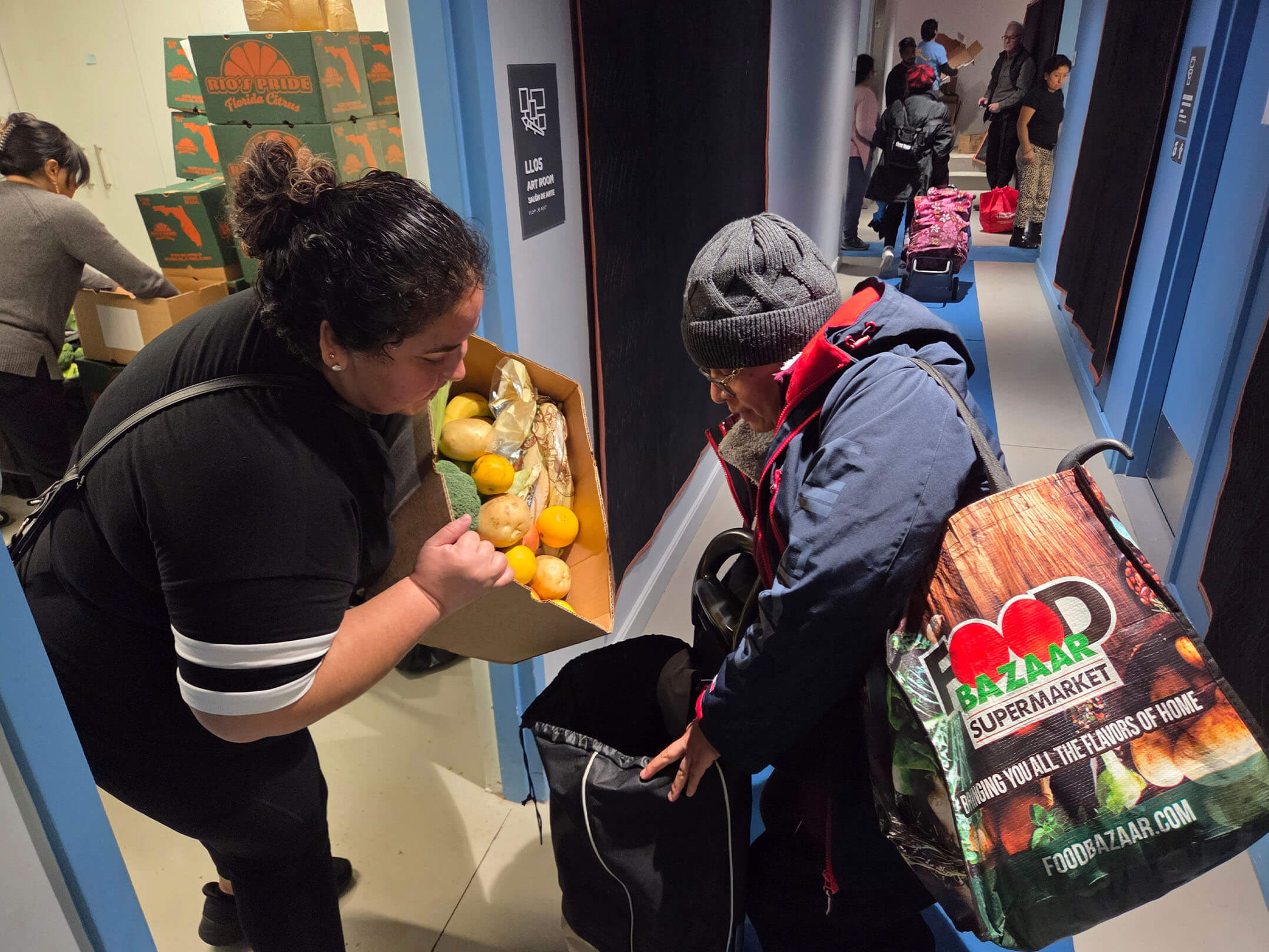 A woman putting fruit into an elderly woman's bag at Make the Road New York's food pantry