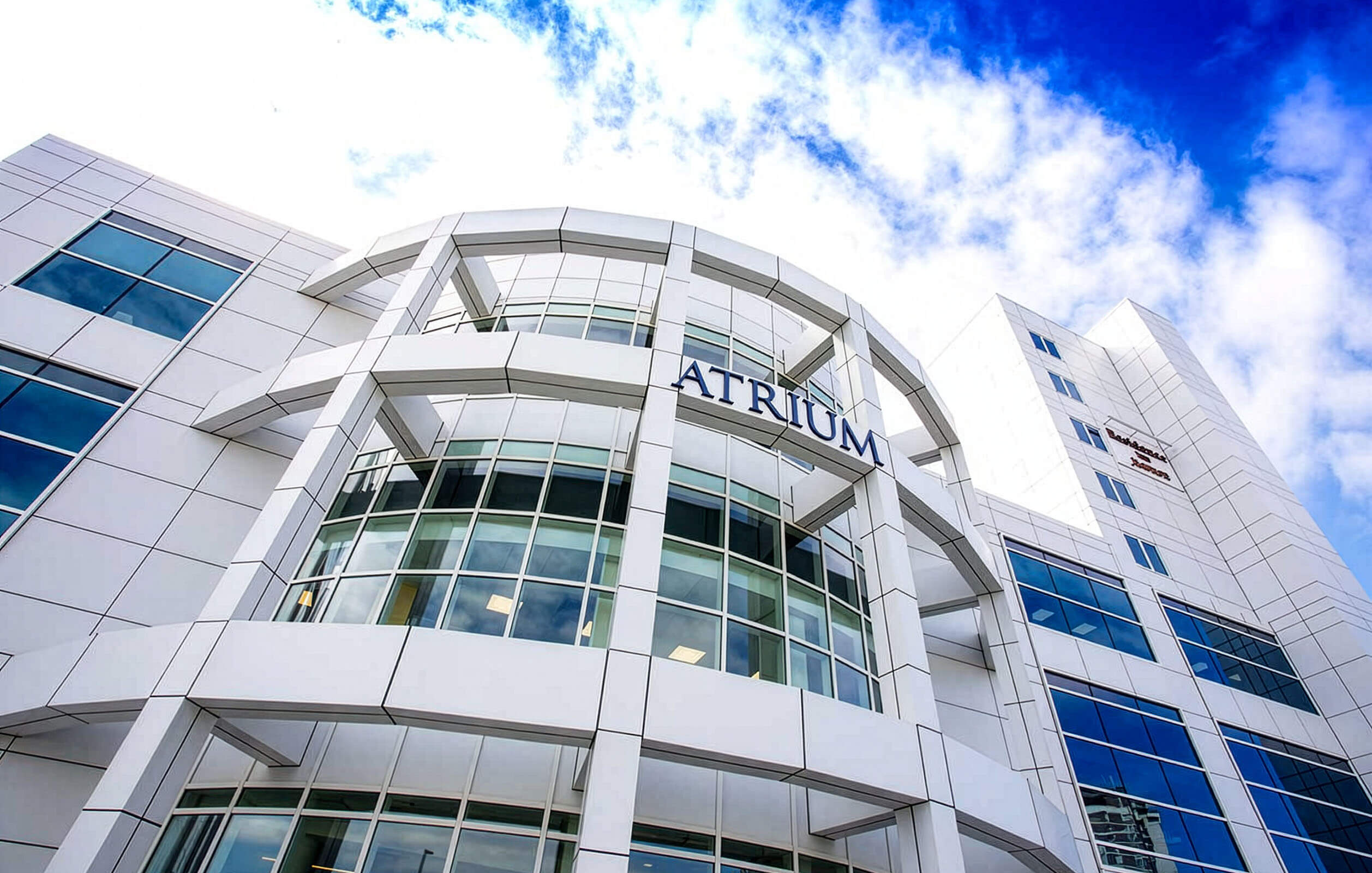 The soaring glass enclosed front entrance of the Metro Center Atrium's office complex outlined by a blue sky and clouds