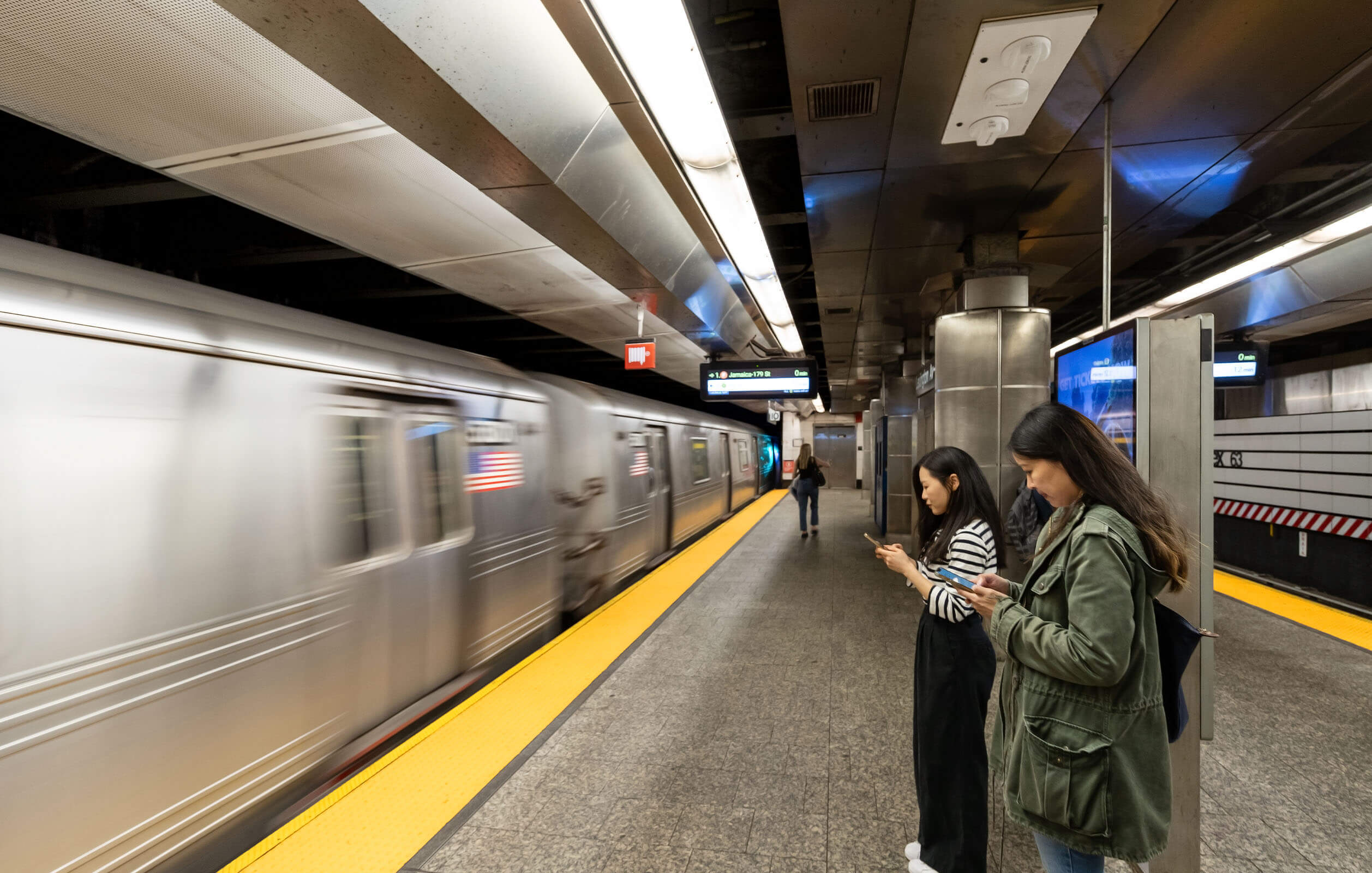 Two women looking at their phones in a subway station in New York City
