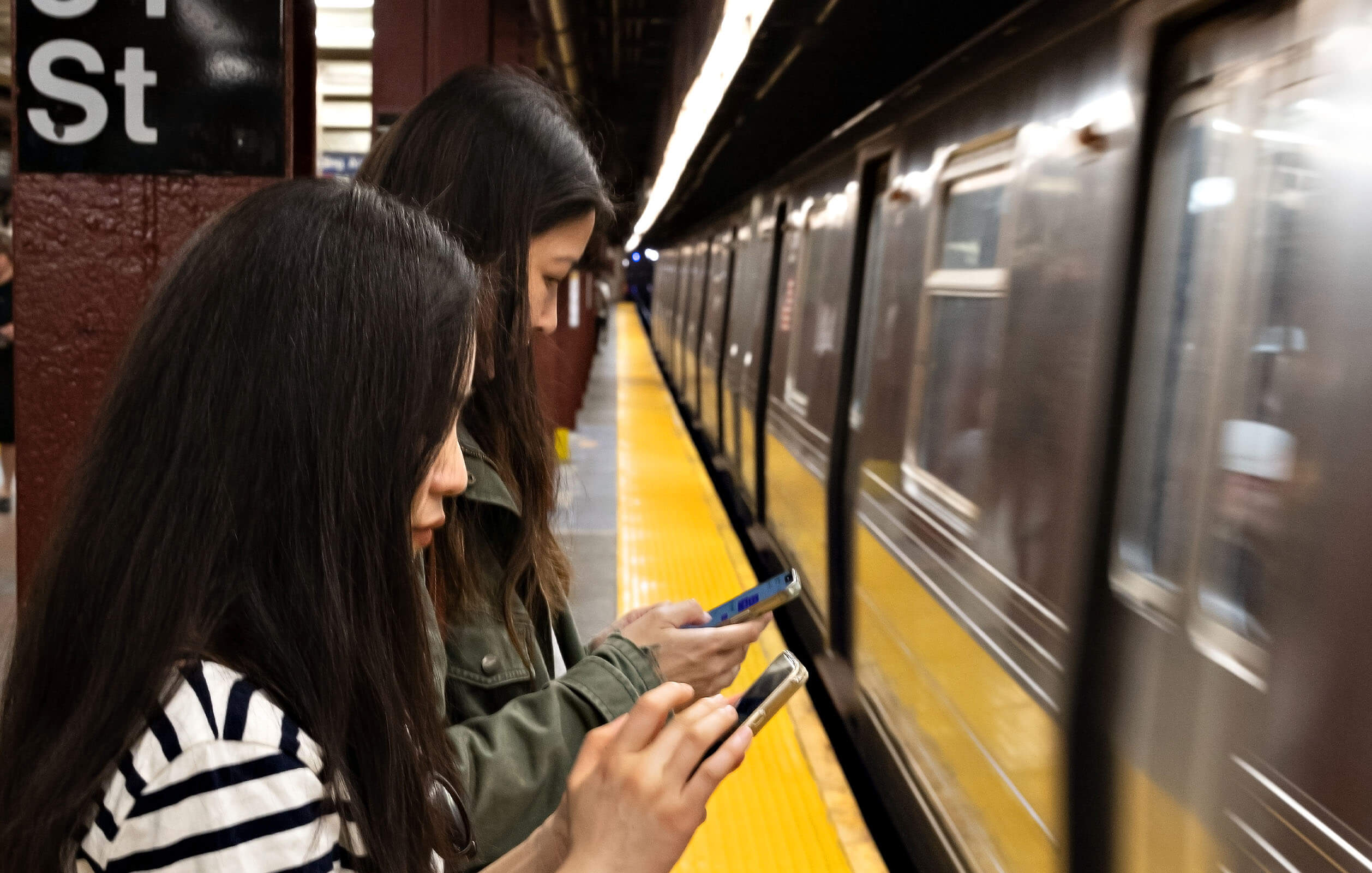 Two women looking at their phones in a subway station in New York City