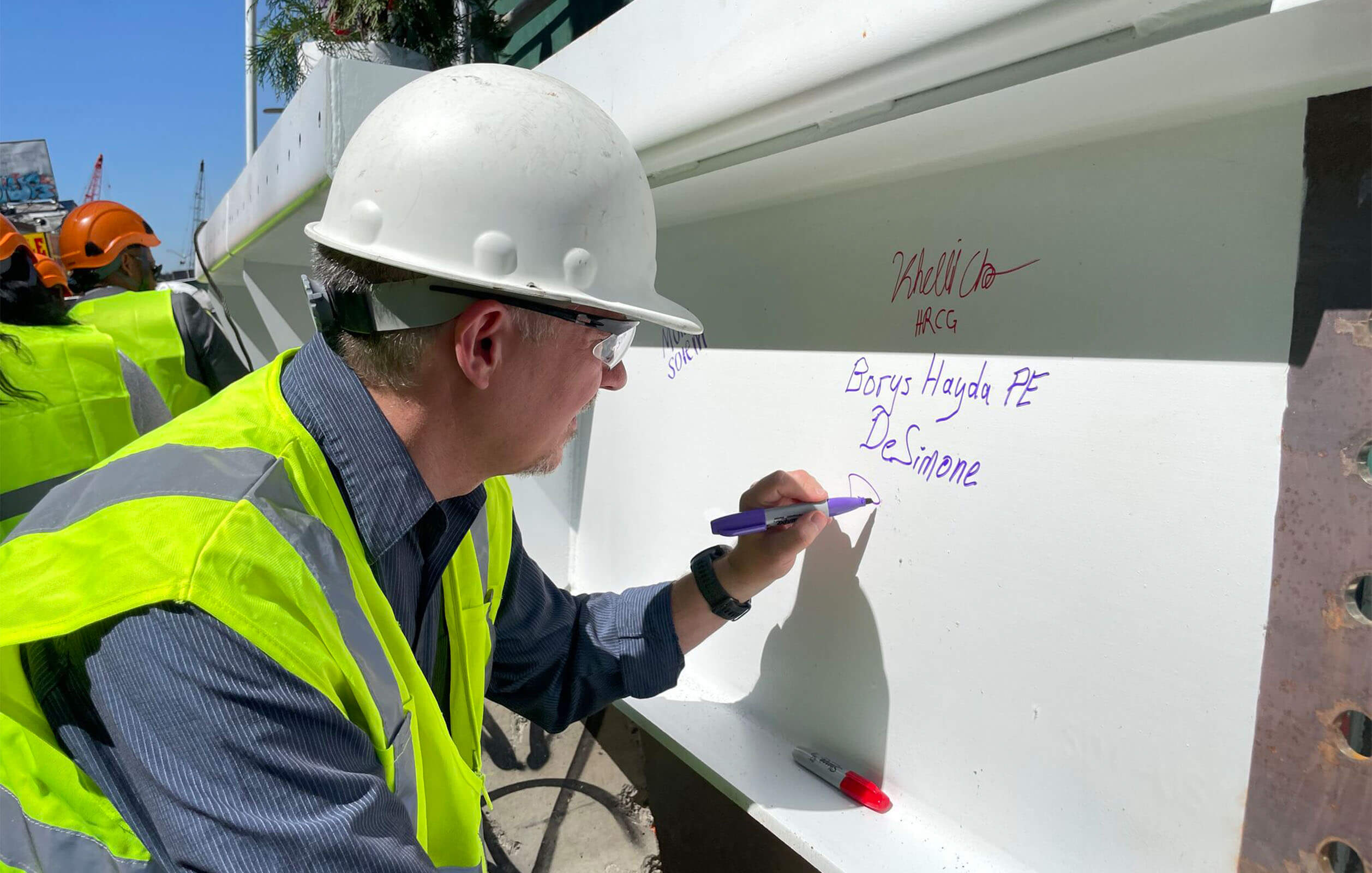 Construction working signing a white steel beam signifiying the topping off of construction of the Kipp NYC charter high school