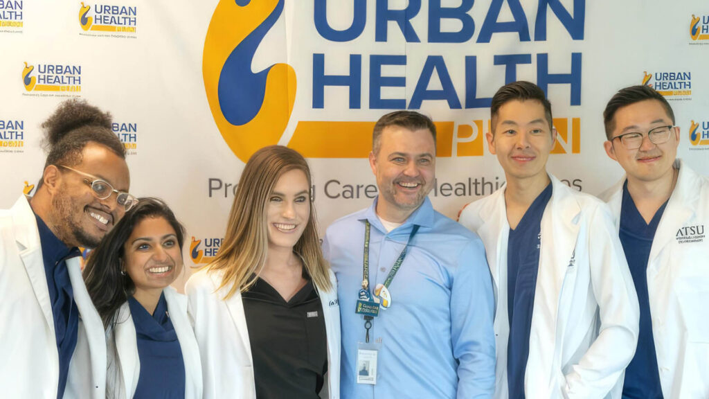 Six young doctors posing in front of Urban Health Plan sign